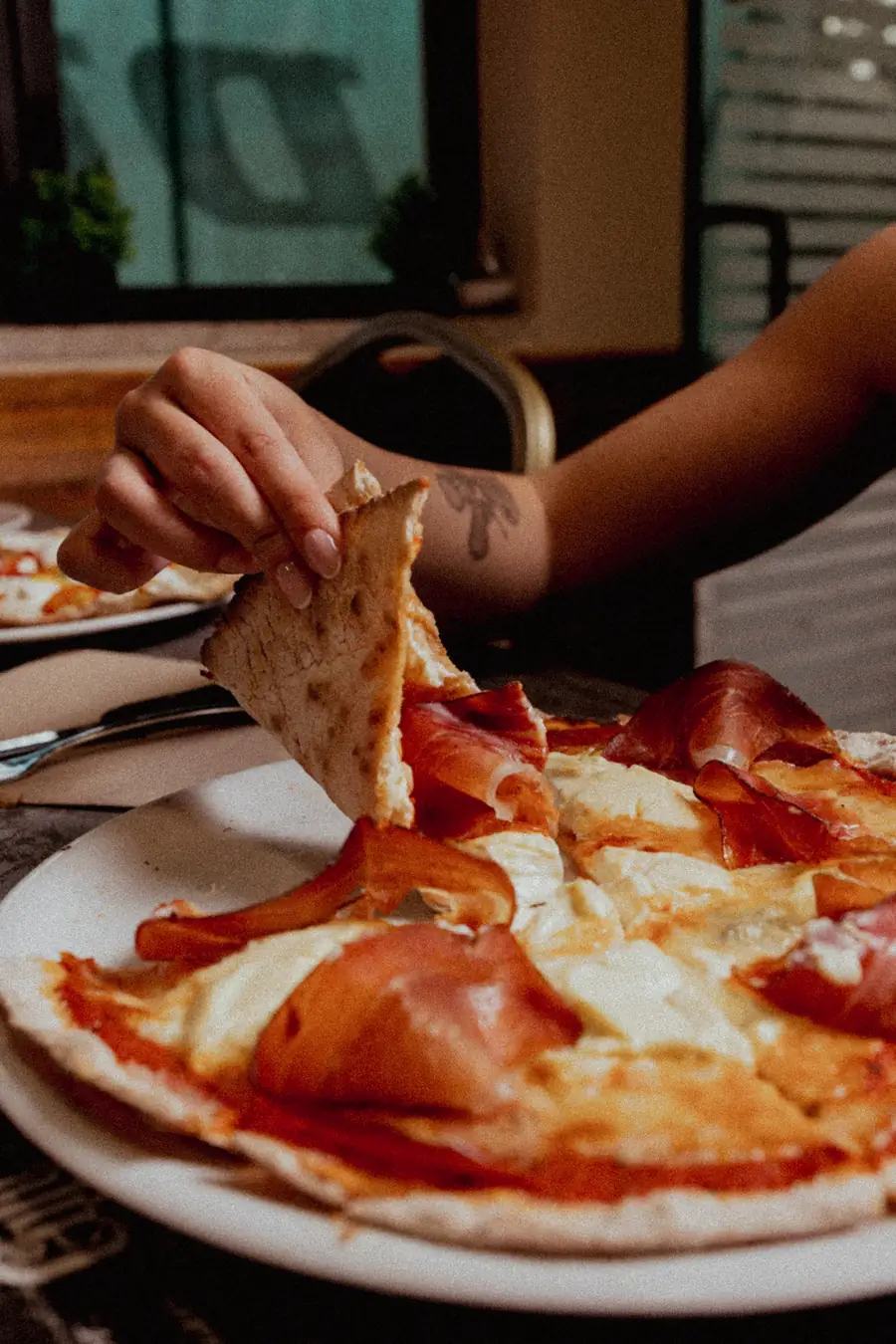 Una fetta di pizza sottile sollevata a mano, che si piega senza spezzarsi